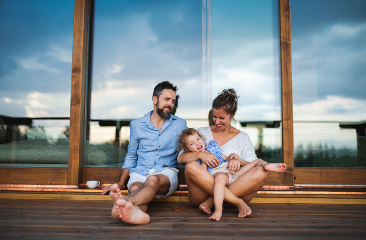 Family with small daughter sitting on patio of wooden cabin, holiday in nature concept.