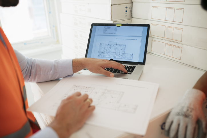 Construction worker and architect reviewing plans together on laptop at site