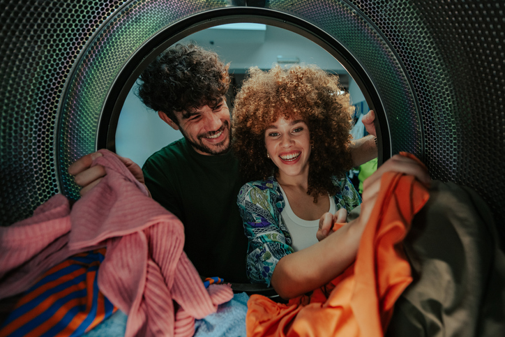 Happy couple loading clothes into washing machine in laundromat